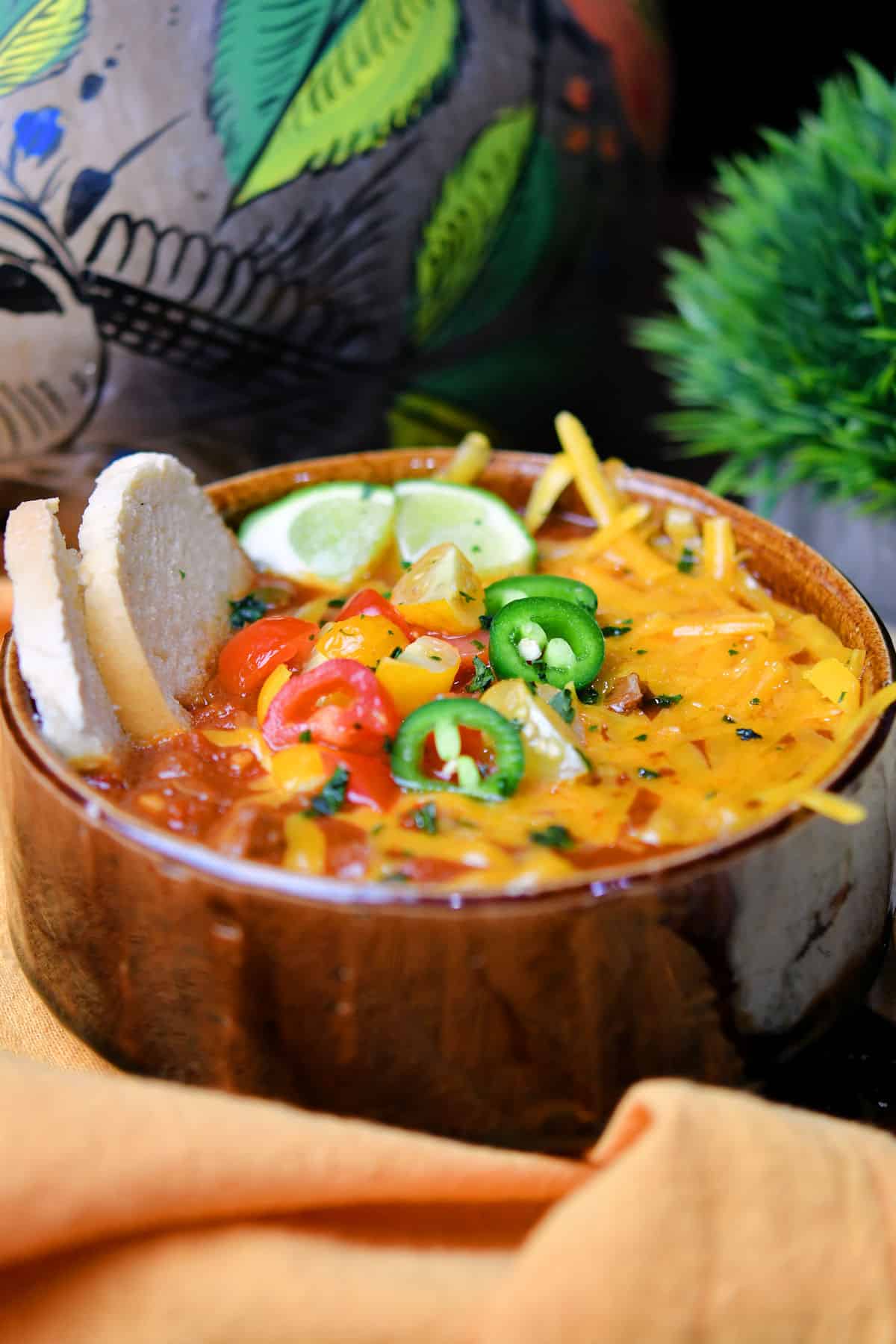 steak chili in a brown bowl with melted cheese, tomatoes and jalapeno slices