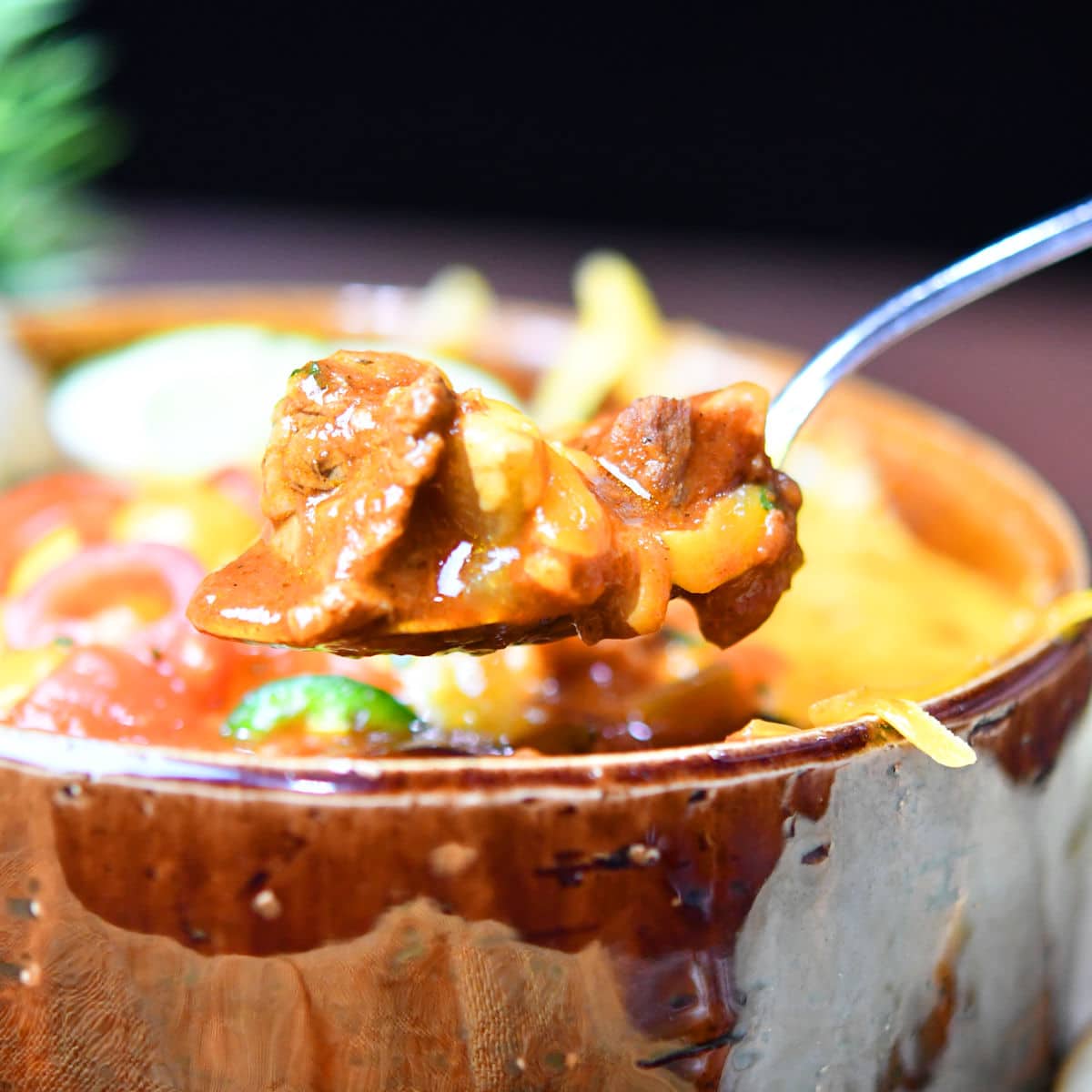 spoonful of steak chili above a brown ceramic bowl