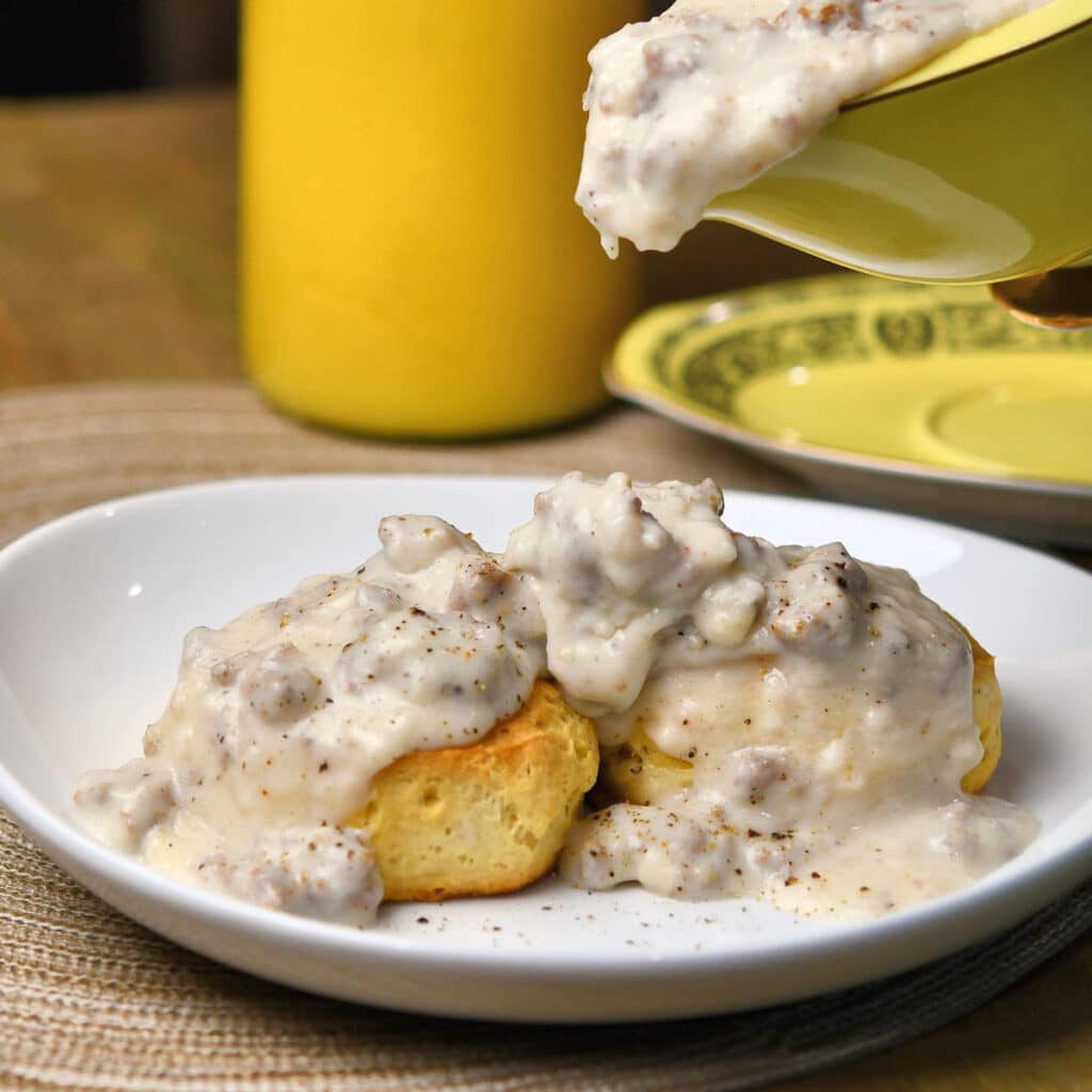 pouring sausage gravy over biscuits on a white plate