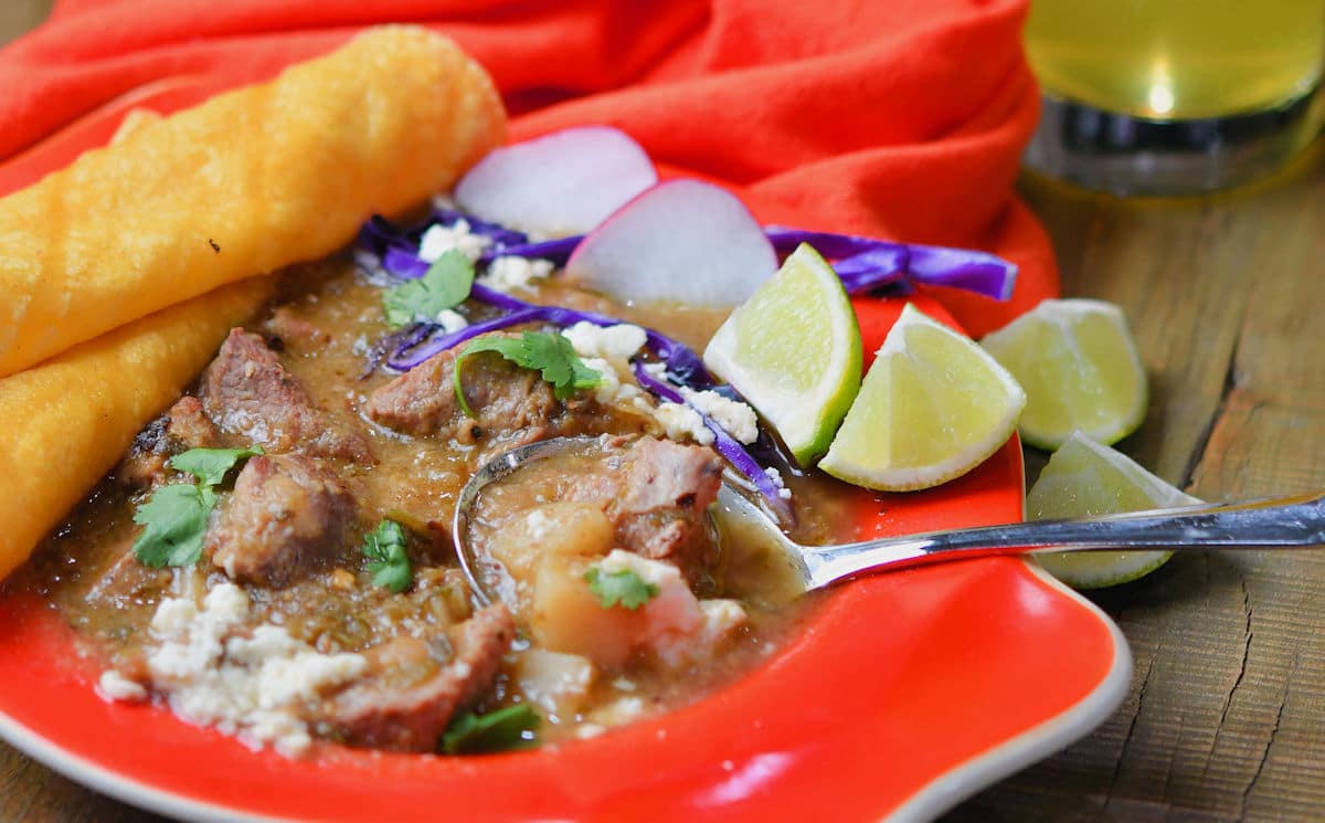 serving of pork guisado with lime wedges, radishes, queso fresco and rolled tortillas