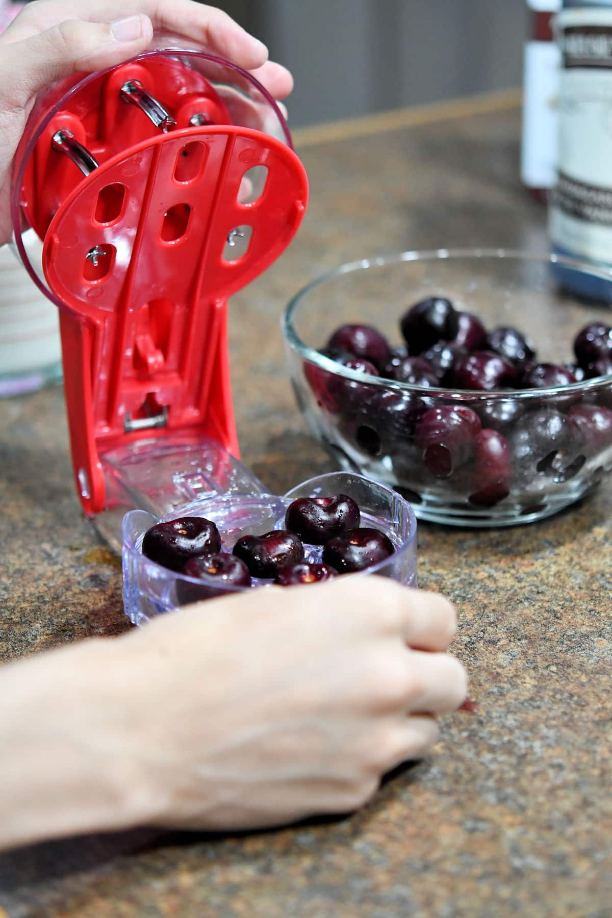 a cherry pitter with a glass bowl of cherries beside it