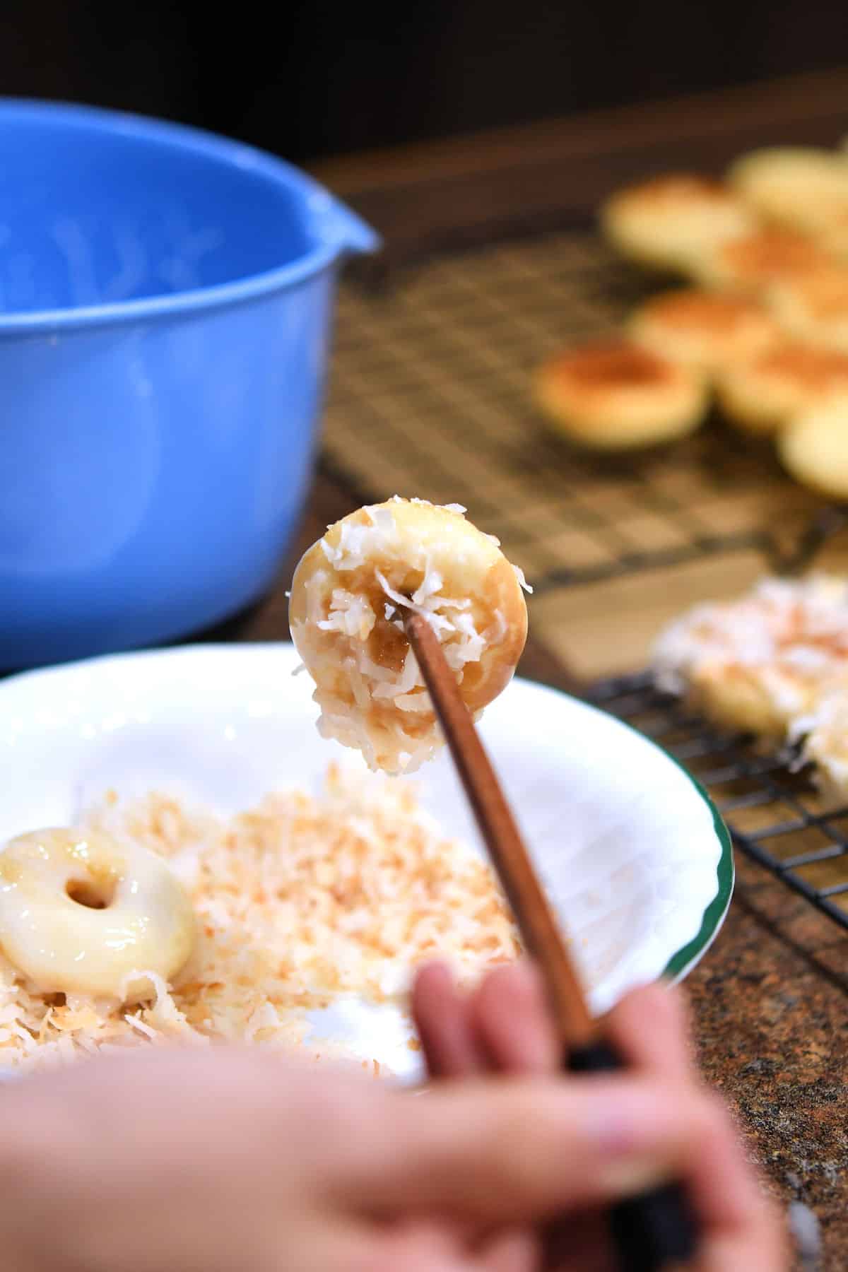 using chopsticks to dip mini donuts into glaze and toasted coconut.