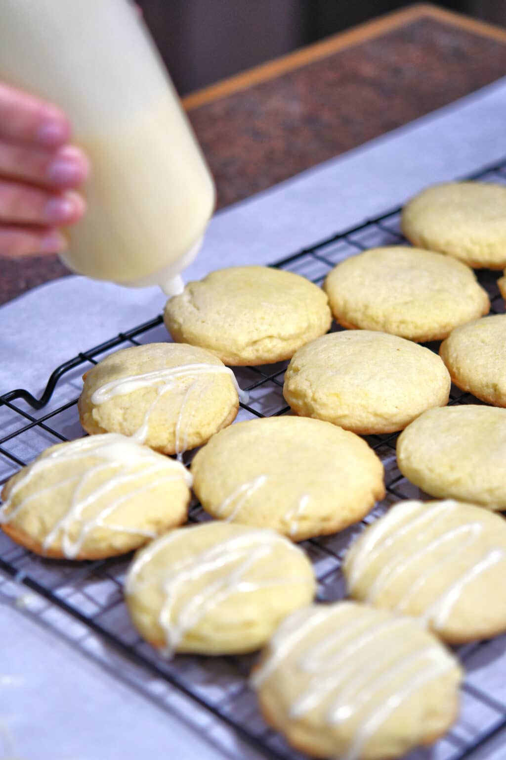 using a squeeze bottle to drizzle melted white chocolate on lemon cookies.