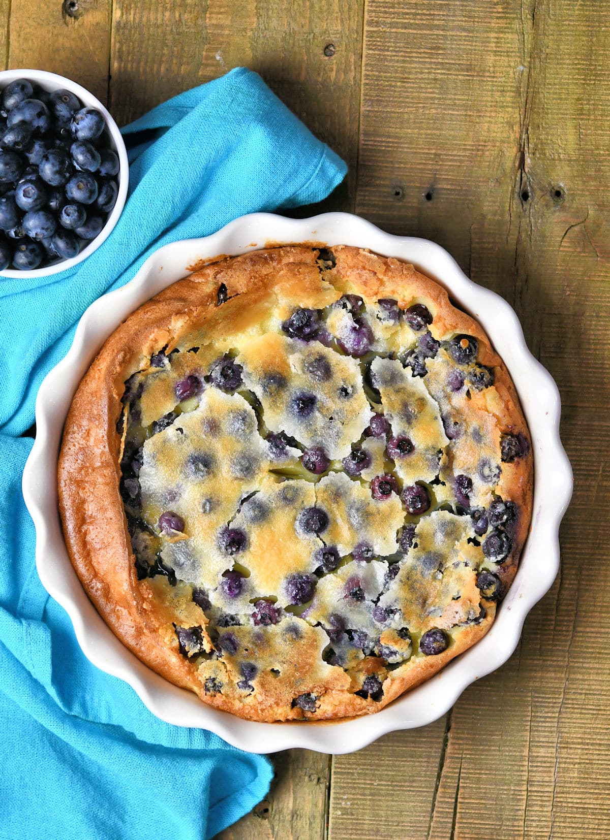 photo of full clafoutis in the pie pan with a bowl of fresh blueberries